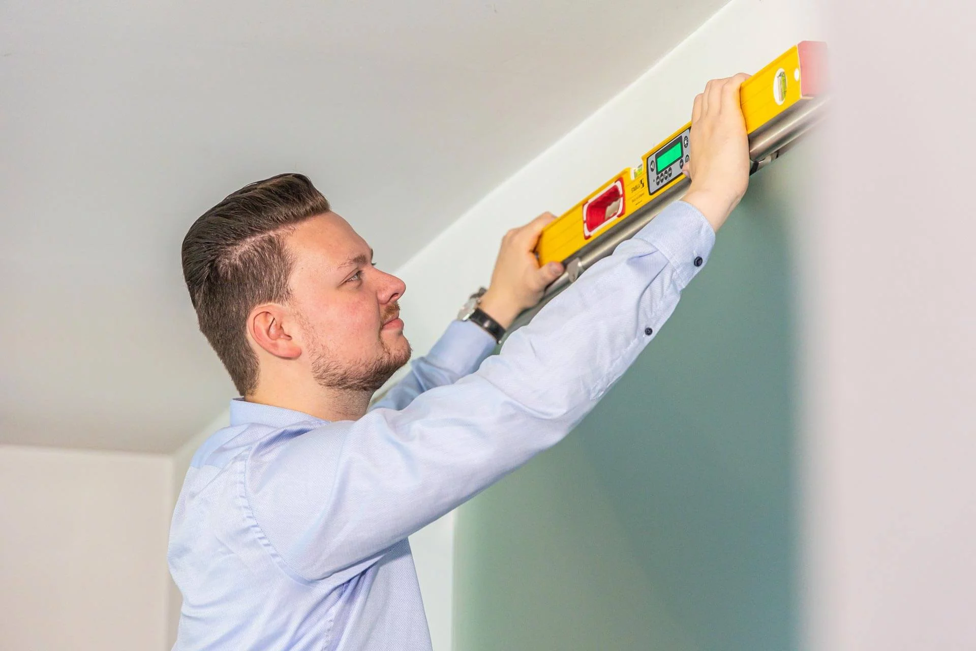 Gero Keuthen mit einer Wasserwaage, die er an eine Wand hält.